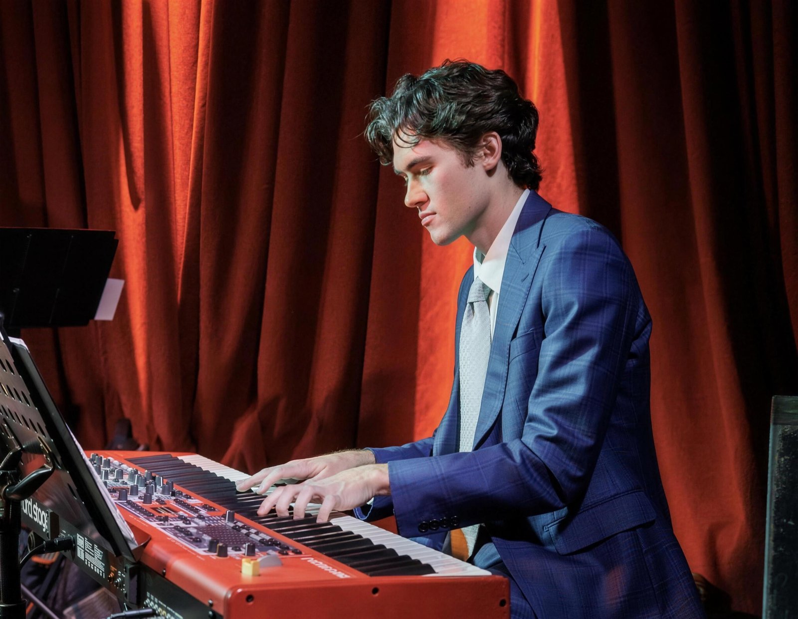 Shane Dickens performing at the piano in front of red stage curtains